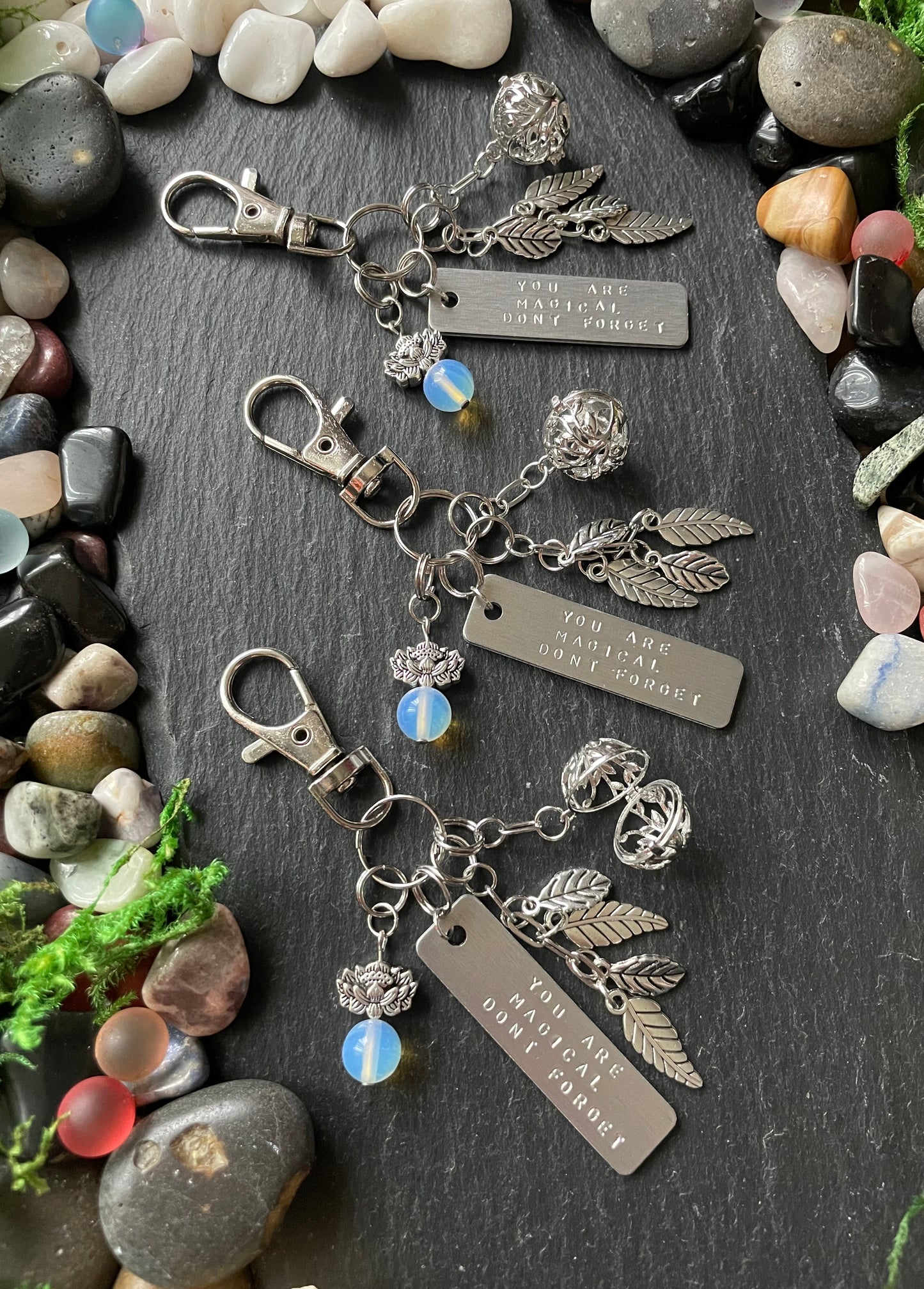 Silver keychain with charms on a dark surface with stones and plants