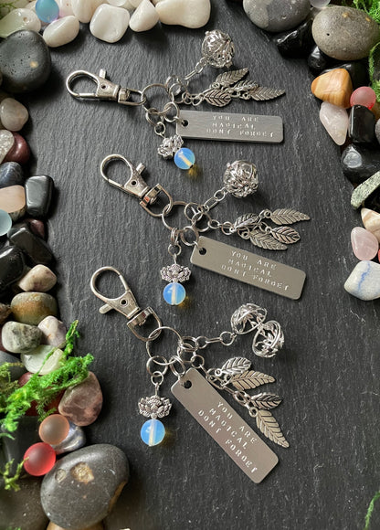 Silver keychain with charms on a dark surface with stones and plants