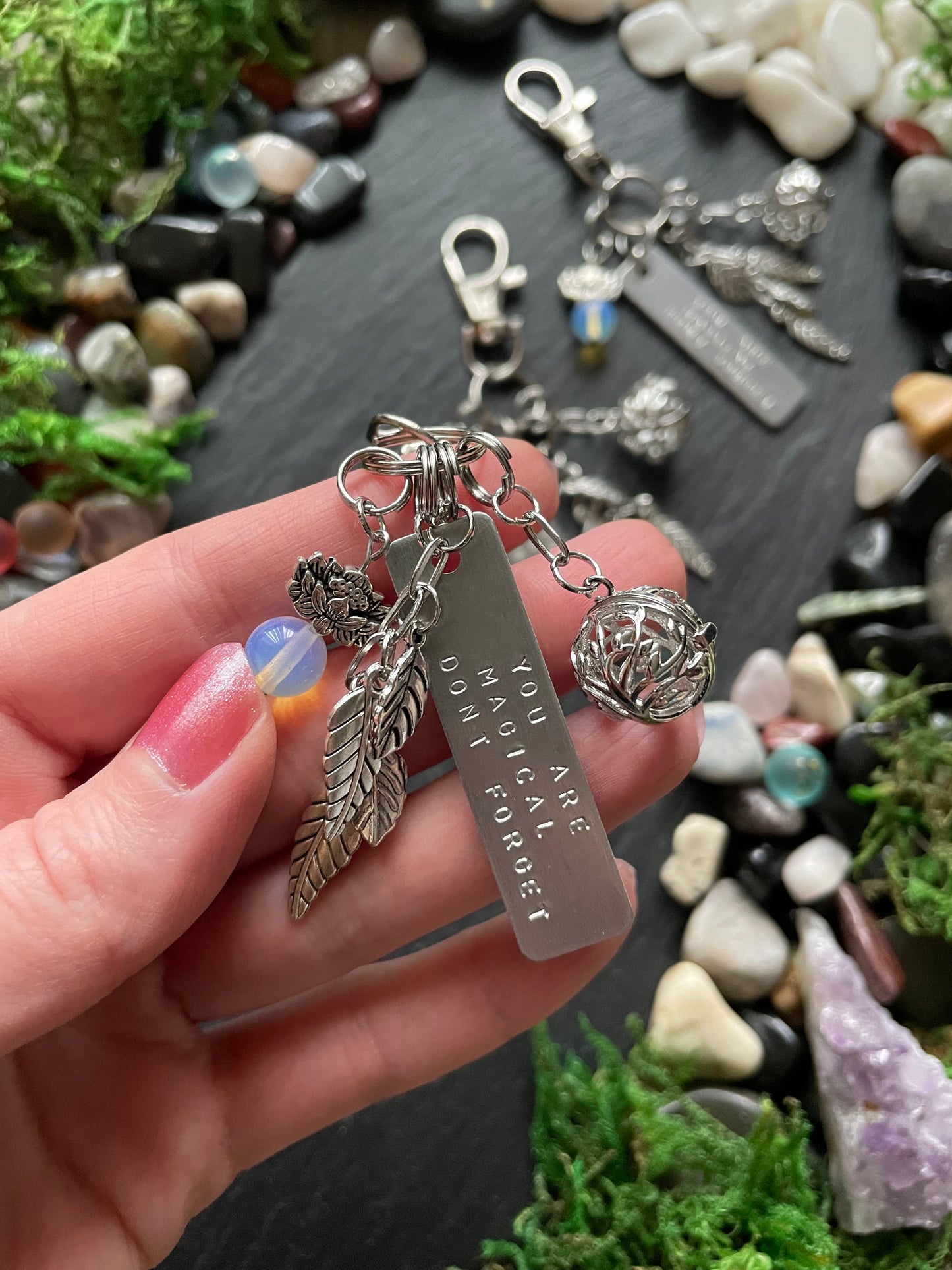 Hand holding a silver keychain with engraved message against a natural stone and moss background