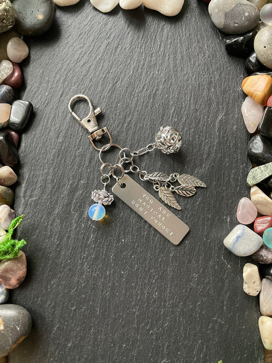 Silver keychain with charms on a dark stone surface surrounded by pebbles.