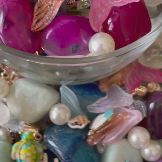 Colorful gemstones and mermaid charms in a wooden bowl