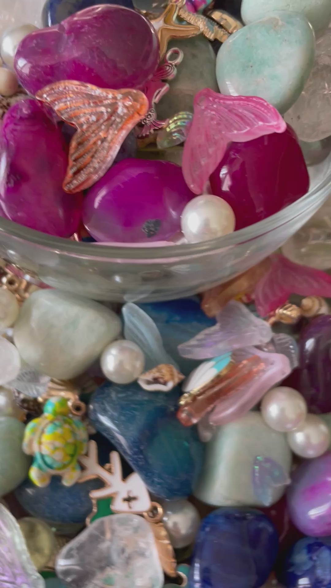 Colorful gemstones and mermaid charms in a wooden bowl