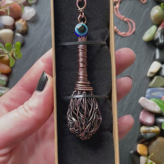 A miniature broom pendant with a blue evil eye bead