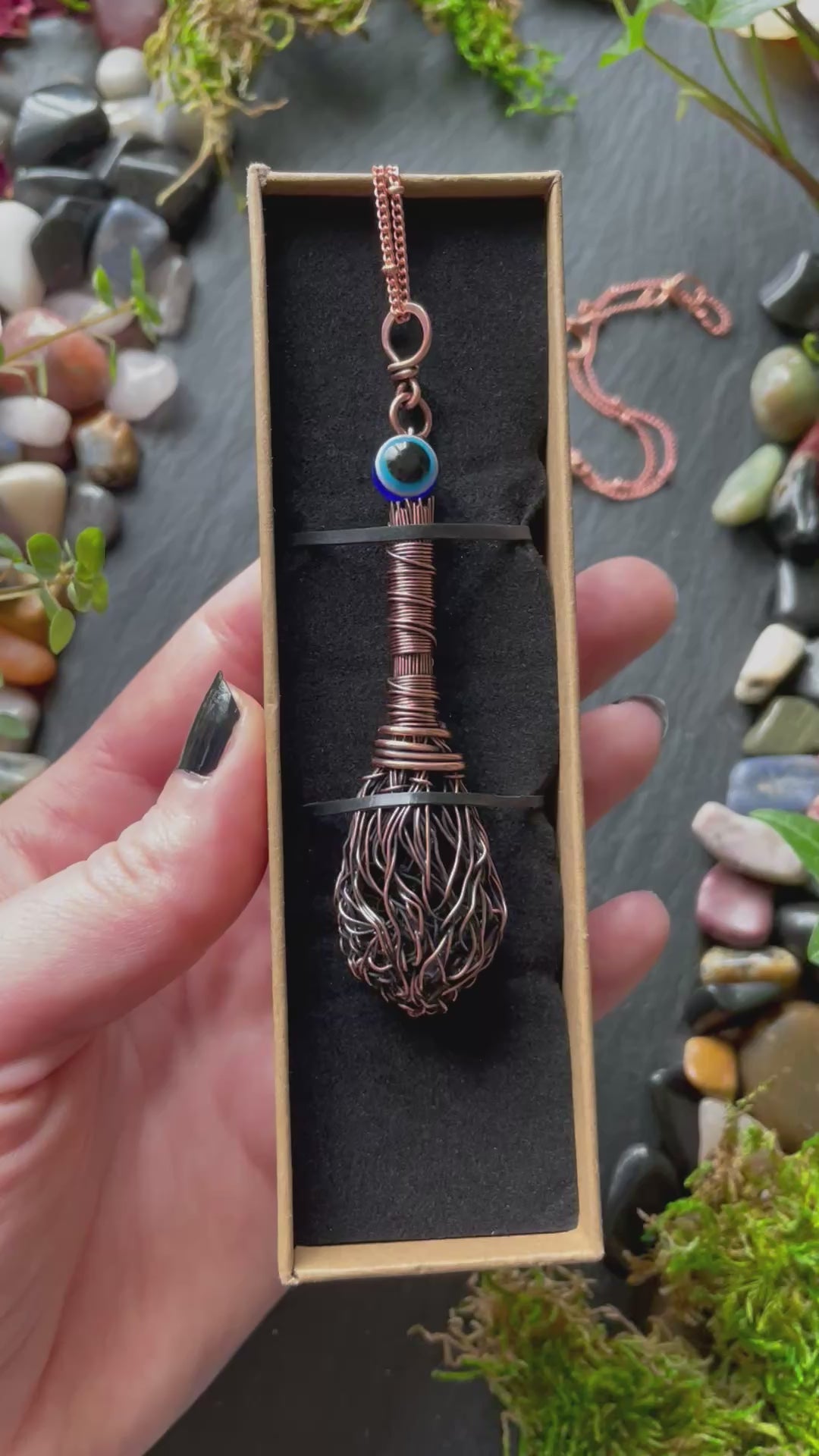 A miniature broom pendant with a blue evil eye bead